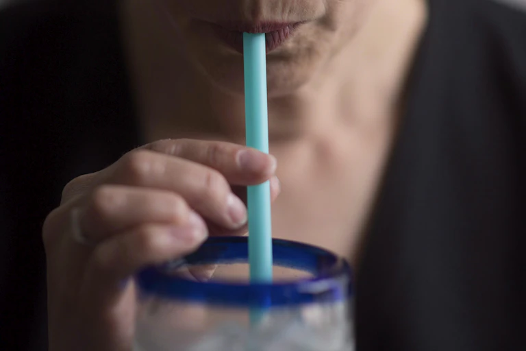 Close up of someone's mouth drinking through a plastic strawn