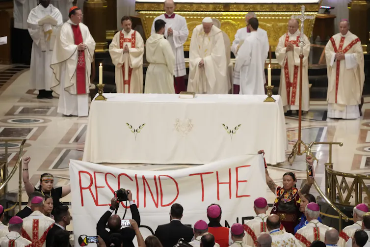 A banner is held up in a church and the words 'rescind the' are seen.