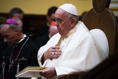 La bandera regresiva para la bandera en la escuela católica establece la reconciliación en la visita posterior a la papina de Canadá 1 Un hombre de blanco con una mano en el pecho.