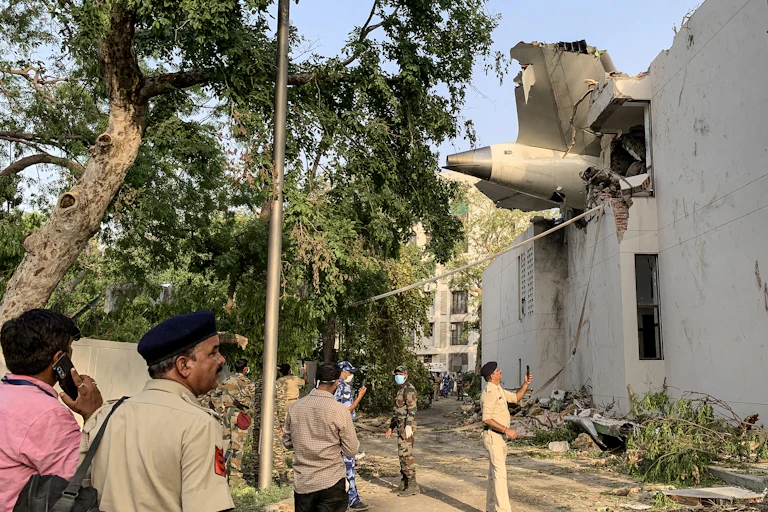 People looking up at the tail of a plane sticking out of an apartment building.