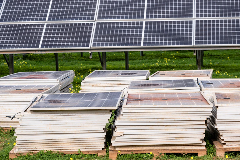 Piles of damaged, old solar panels on the ground with a new system in the background.