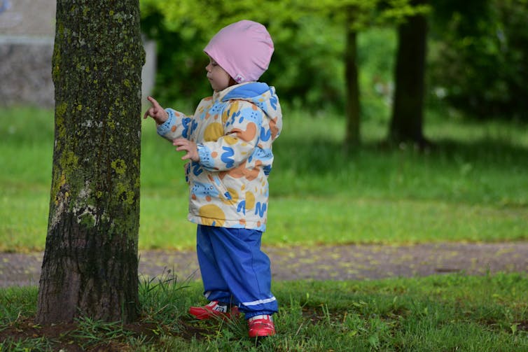 small child standing next to tree in park