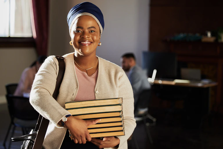 Smiling young woman carrying a pile of books