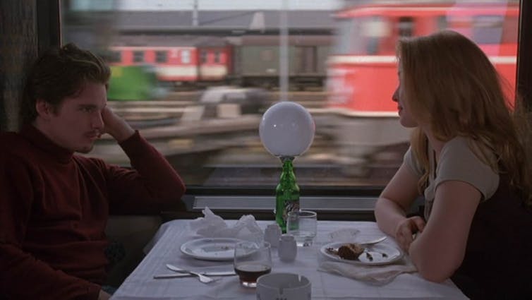 Un chico y una chica se sientan frente a frente en el vagón restaurante de un tren.