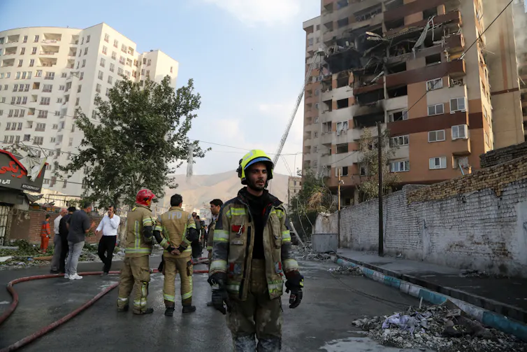 A man in firefighters garb walks downa. street strewn with debris.