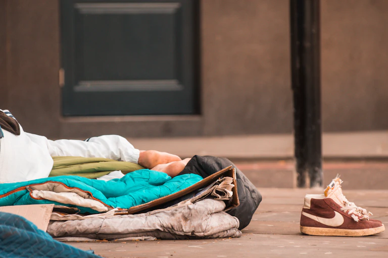 Close up of feet of a man sleeping rough, with trainers placed beside him