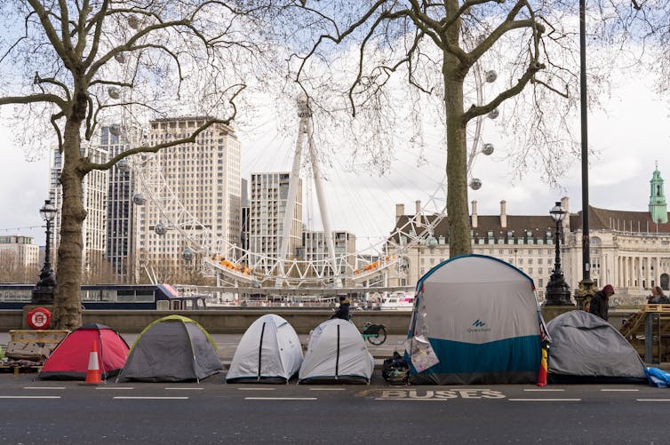 A row of tents on London's embankment, with the London Eye visible in the background