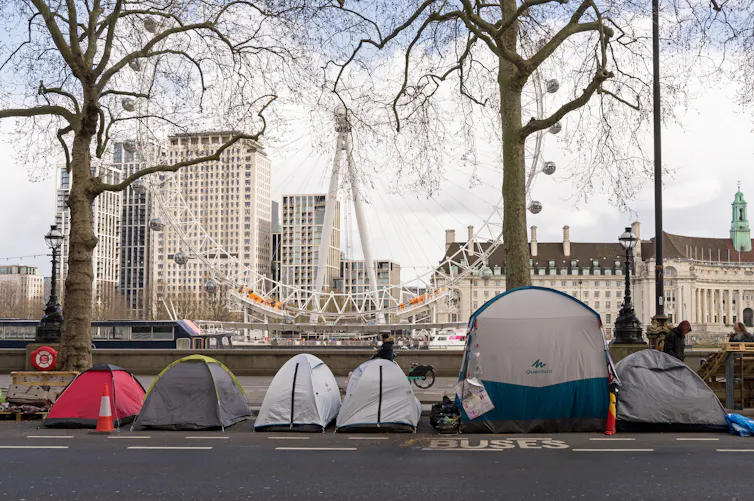 A row of tents on London's embankment, with the London Eye visible in the background
