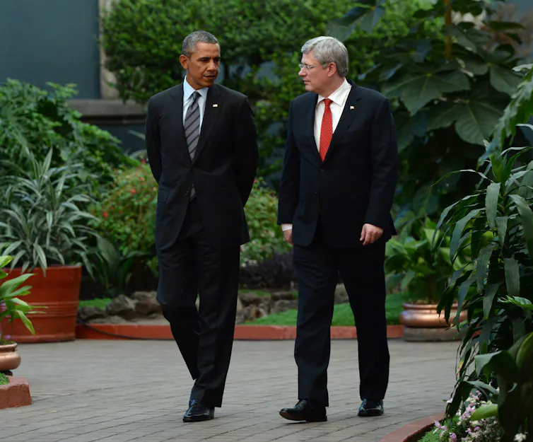 a white man with grey hair walks talking to a tall thin black man