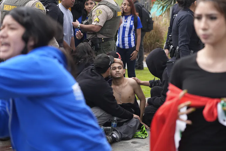 an injured young man sits on the ground as people tend to him