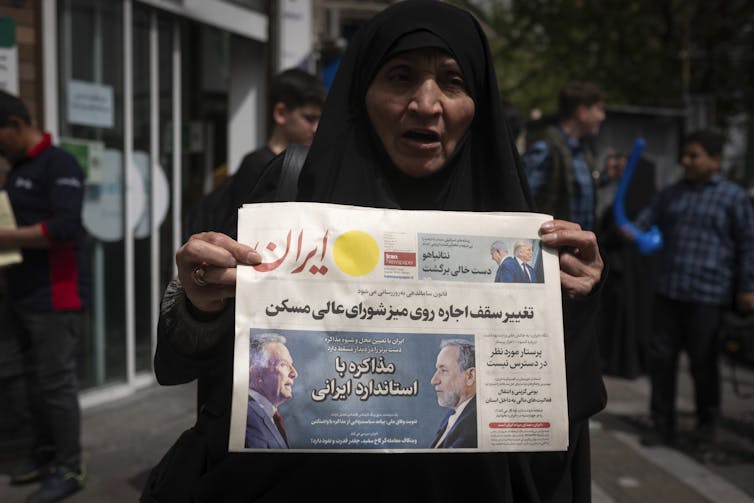 A woman holds a newspaper with Iranian writing and a photo of two men.