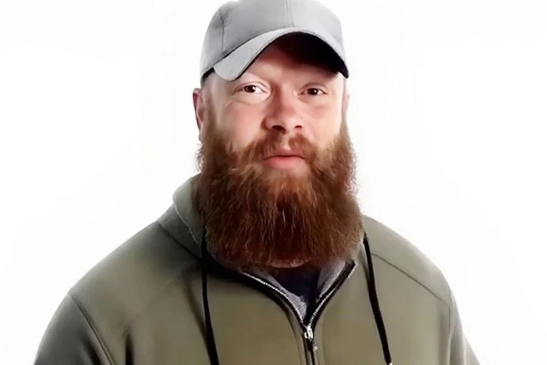 a bearded man wearing a sweatshirt and ball cap