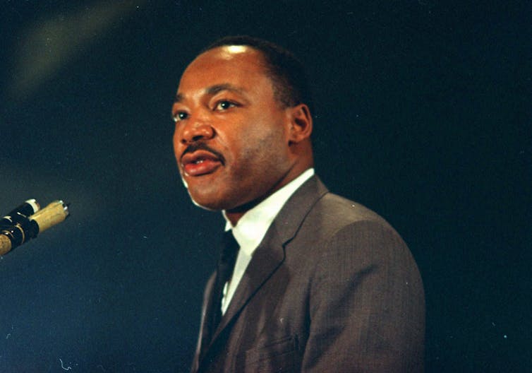 a man in a suit and tie stands in front of a microphone