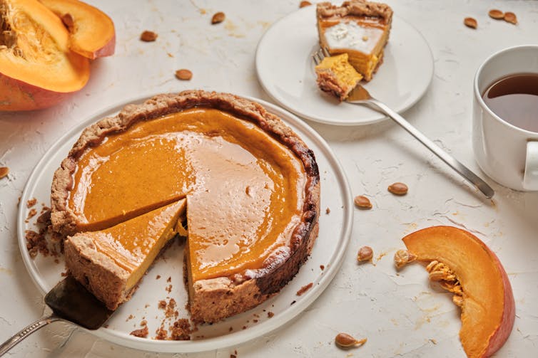 A pumpkin pie sits on a table with a couple of slices cut from it.