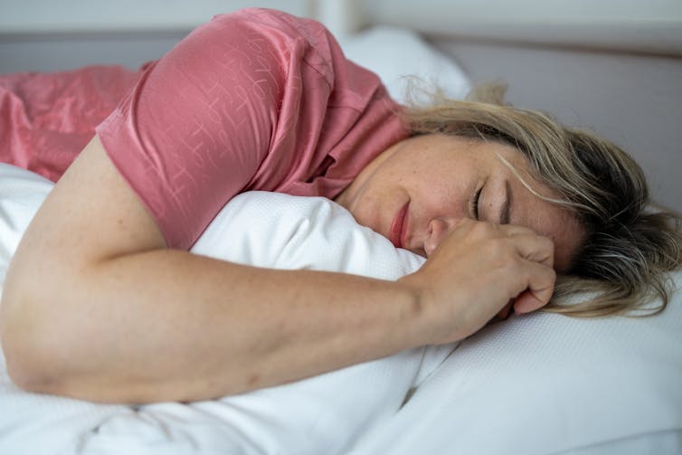 Person lying on side in bed, eyes closed, possibly grimacing