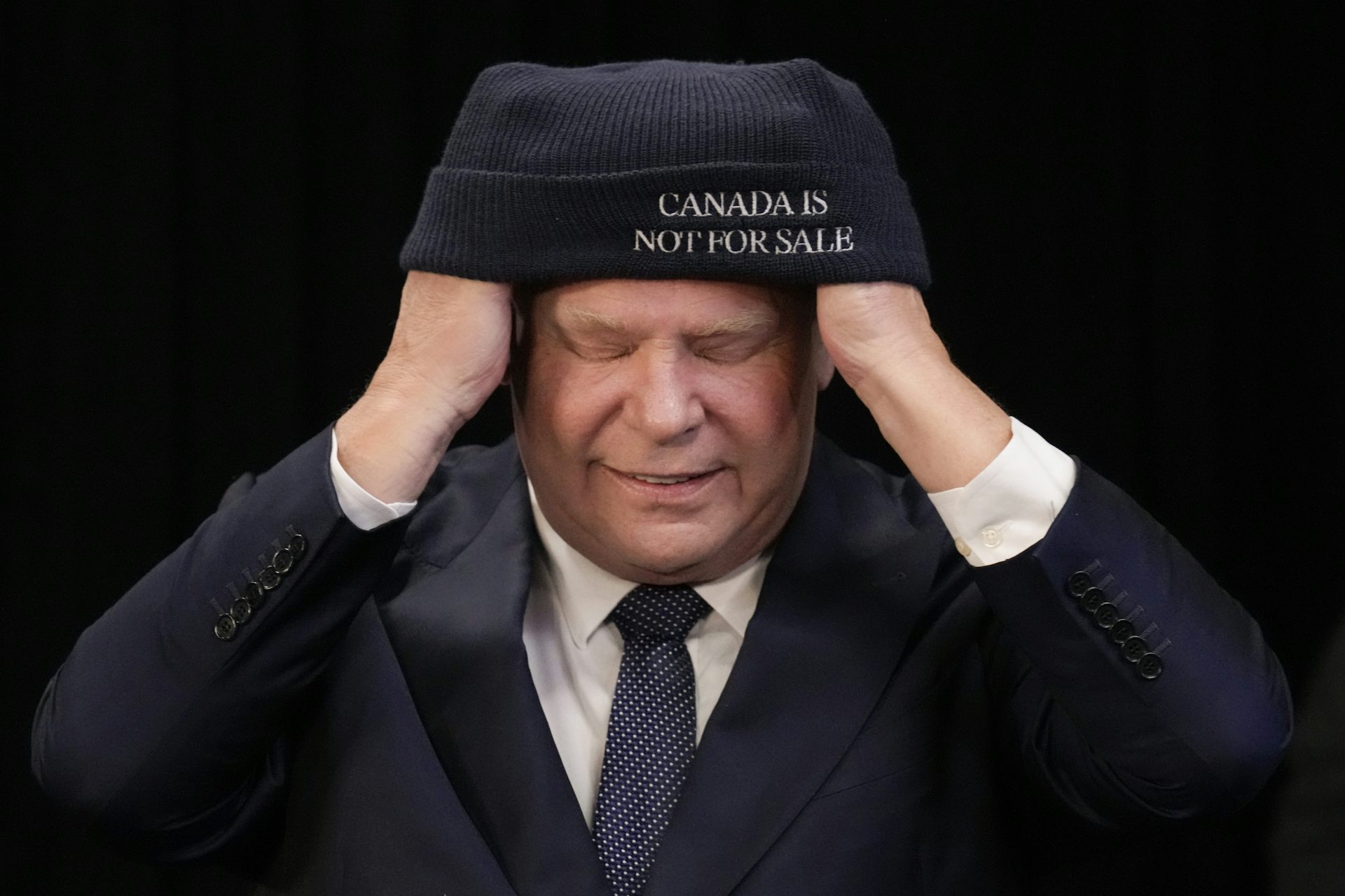 A man has his eyes closed and is putting on a toque that says 'Canada is not for sale.'