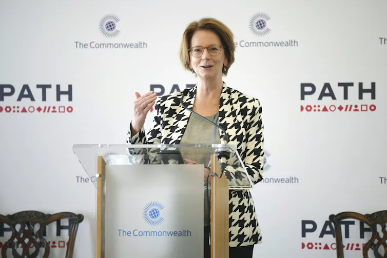 A woman with a short bob in a houndstooth blazer speaks from behind a podium
