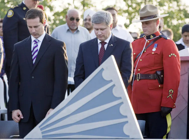 Two men in suits stand next to a man in a red uniform; all have their heads bowed