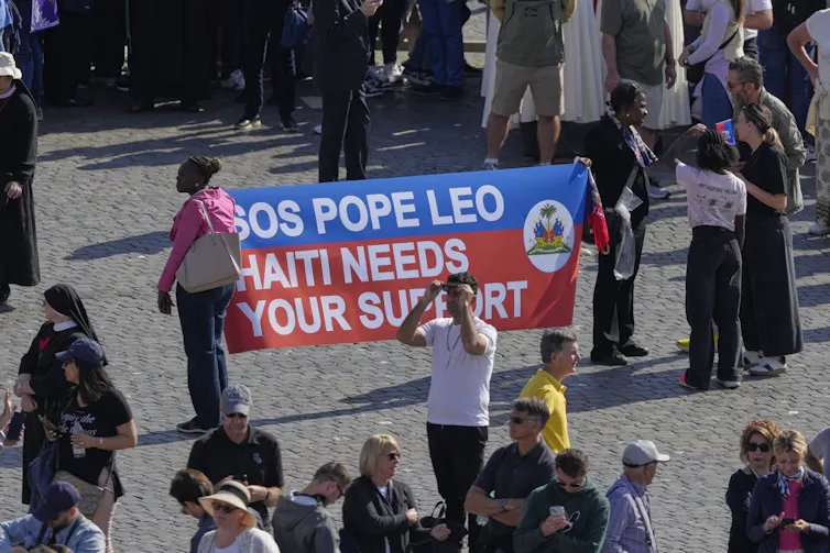 people hold up a sign in a square that says 'Pope Leo: Haiti needs your support'