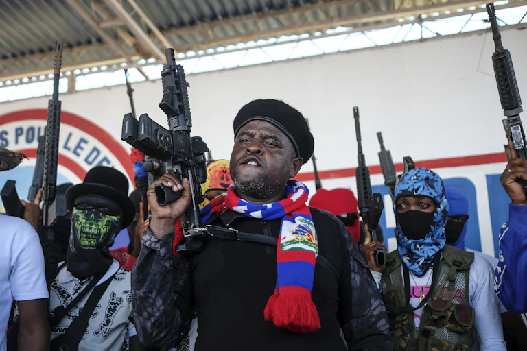 a man holds up an automatic weapon. several people behind him do the same; most wear masks
