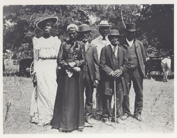 A group of people in fancy dress from the turn of the 19th century, standing together outside.