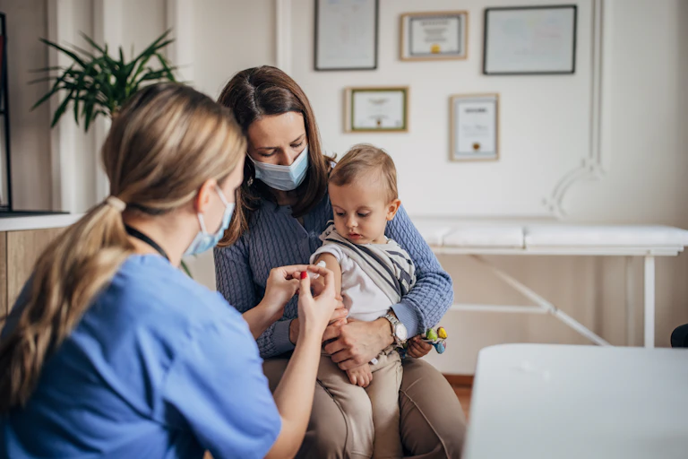 A mother holds a small boy on her lap while a nurse administers a vaccination.
