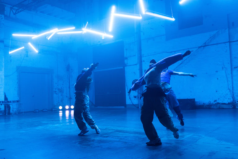 Three dancers under neon blue lights.