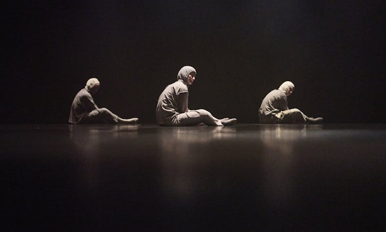 Three people sit on stage in grey tracksuits.