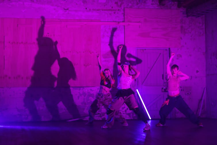 Three dancers under neon purple lights.