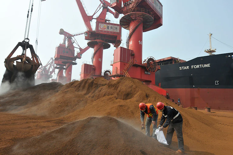 Two men inspecting a pile of iron ore on front of a ship