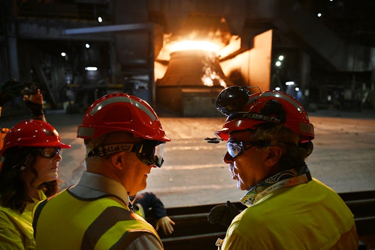 three people in protective clothing in front of steel furnace