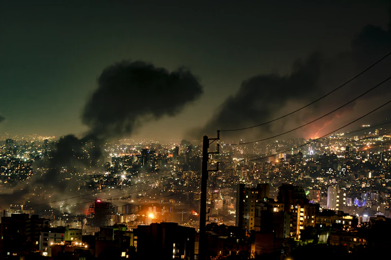 Smoke rises in the night sky above a city.