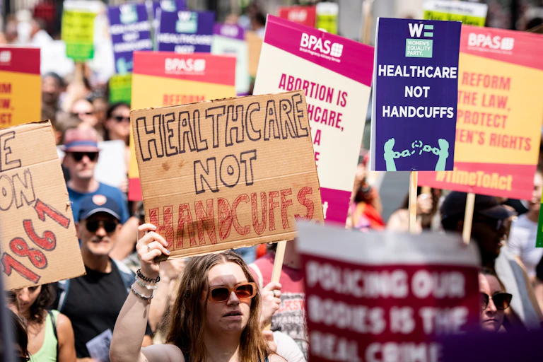 protesters carrying signs, the most prominent in the photo reads 'healthcare not handcuffs'
