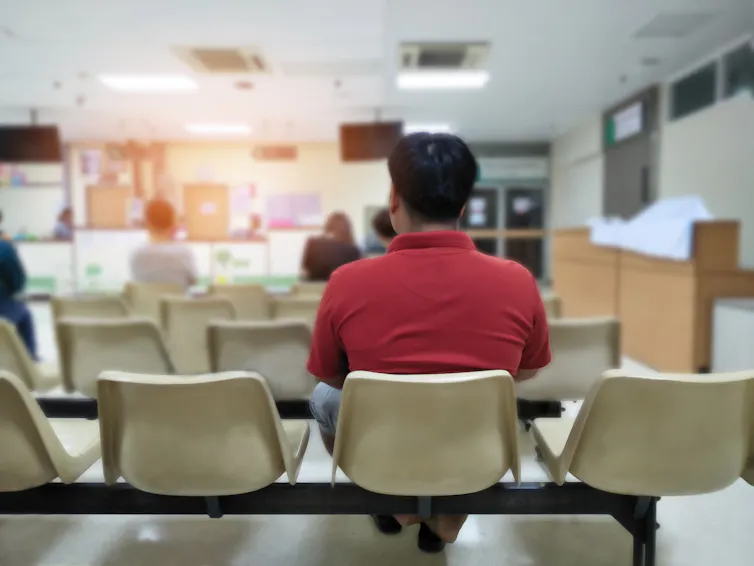 man in a red shirt seen from behind sitting in a hospital waiting room.