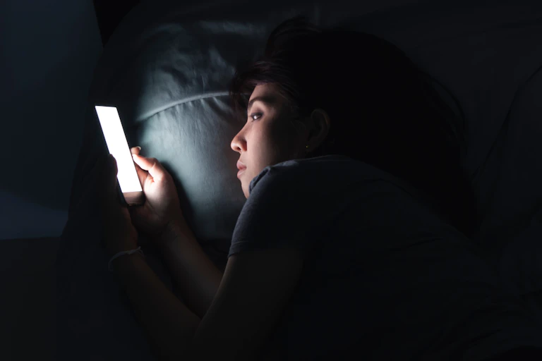 Une jeune femme consulte son écran de téléphone, la nuit, dans son lit