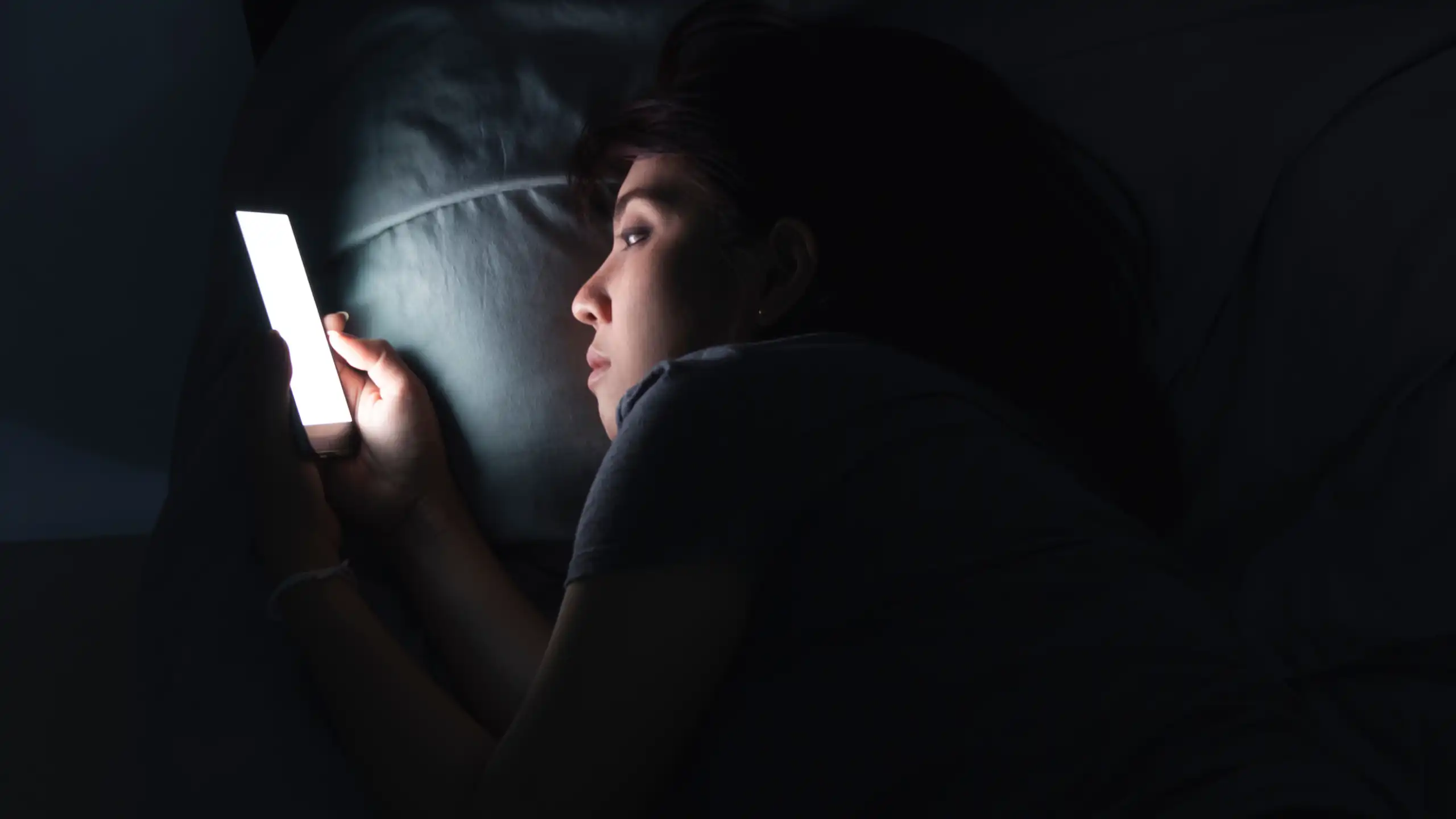 Une jeune femme consulte son écran de téléphone, la nuit, dans son lit