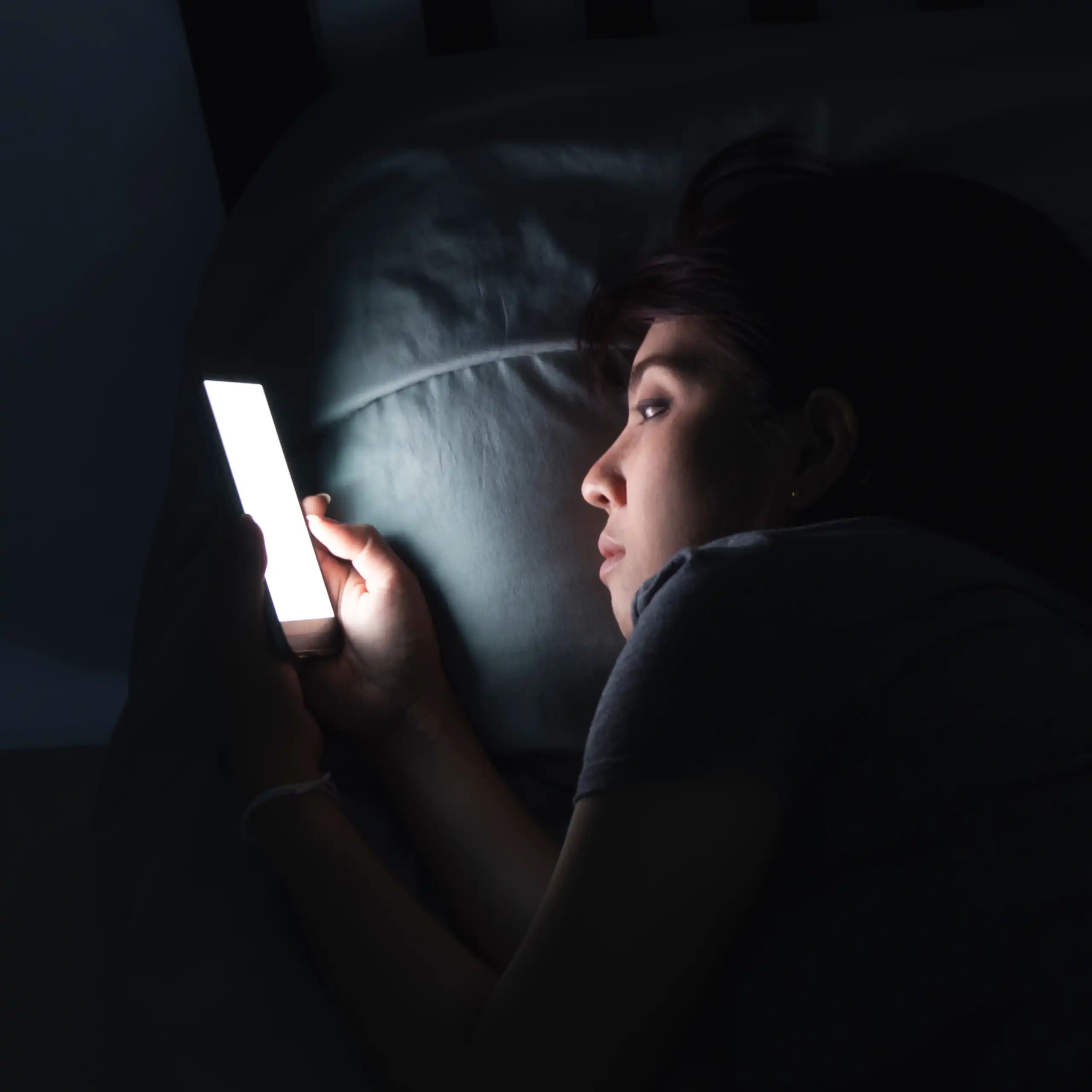 Une jeune femme consulte son écran de téléphone, la nuit, dans son lit