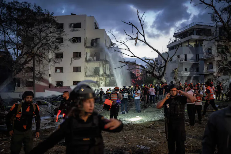Israeli security and emergecy workers at the site of a missile strike as morning breaks over Tel Aviv, June 16 2025.