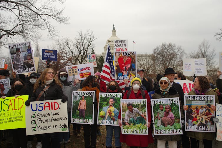 How assist cuts is also affecting humanitarian employees 1 Protesters with signs featuring photos of aid workers that read 'the faces of foreign aid'