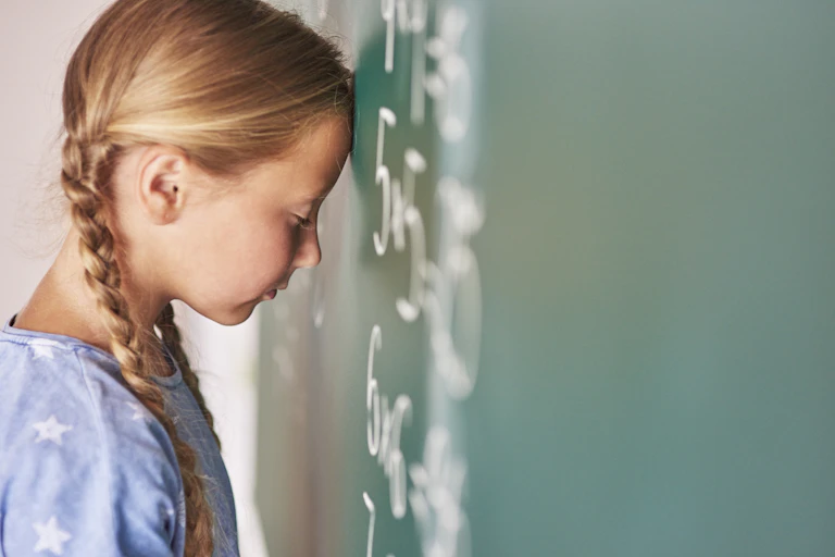 Una niña apoya la cabeza en una pizarra con fórmulas matemáticas