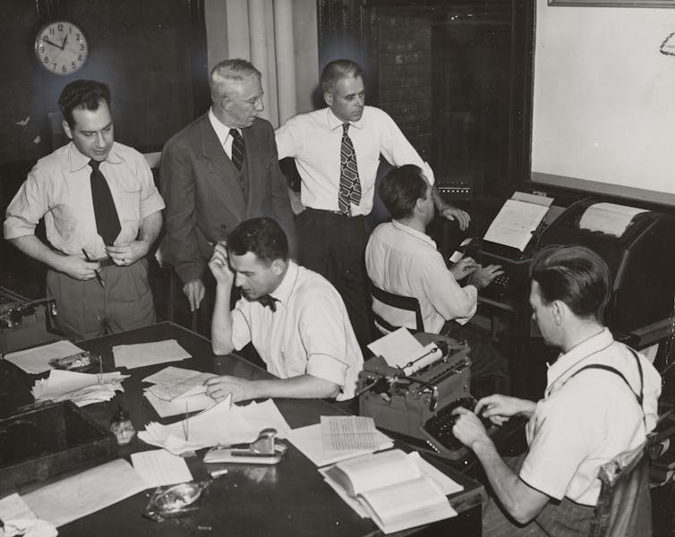 Fundaciones de la comunidad canadiense se morta para apoyar las noticias locales, invitándola a lo esencial para la democracia 2 Imagen en blanco y negro de seis hombres con camisetas y relaciones blancas. Uno lleva un traje para un traje. Dos golpes, uno está leyendo.