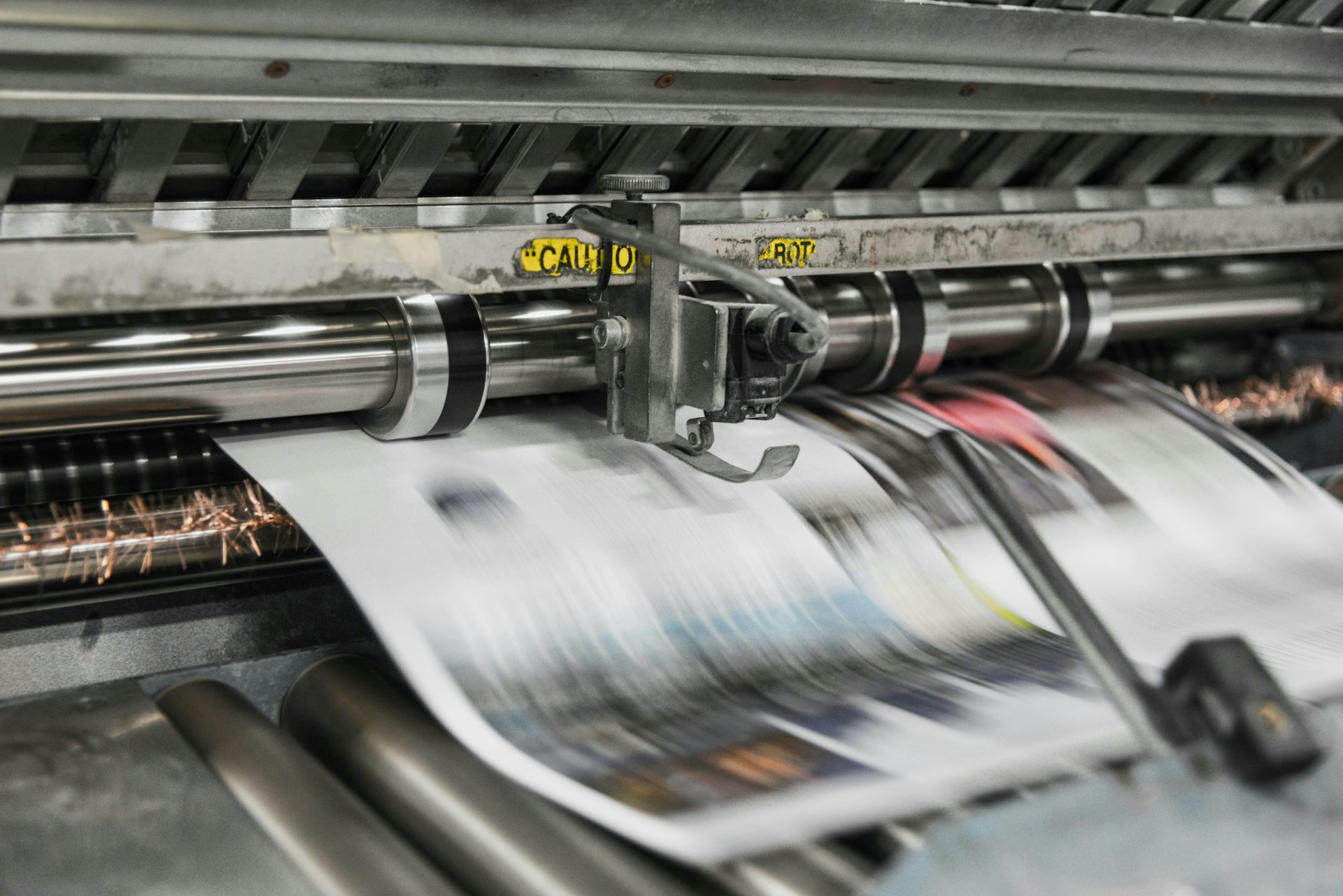 a close up of a blurred newsprint inbetween a roller in a silver machine