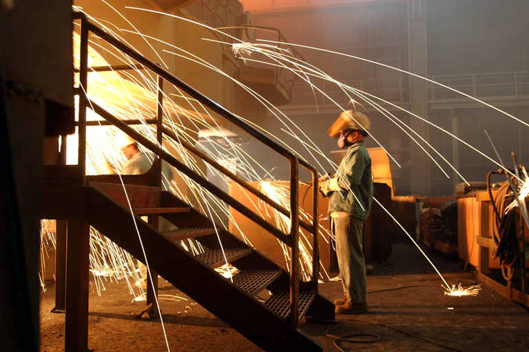 A worker is surrounded by sparks from molten steel flowing into casts at the TAMCO steel mill on October 4, 2002 in Rancho Cucamonga, California