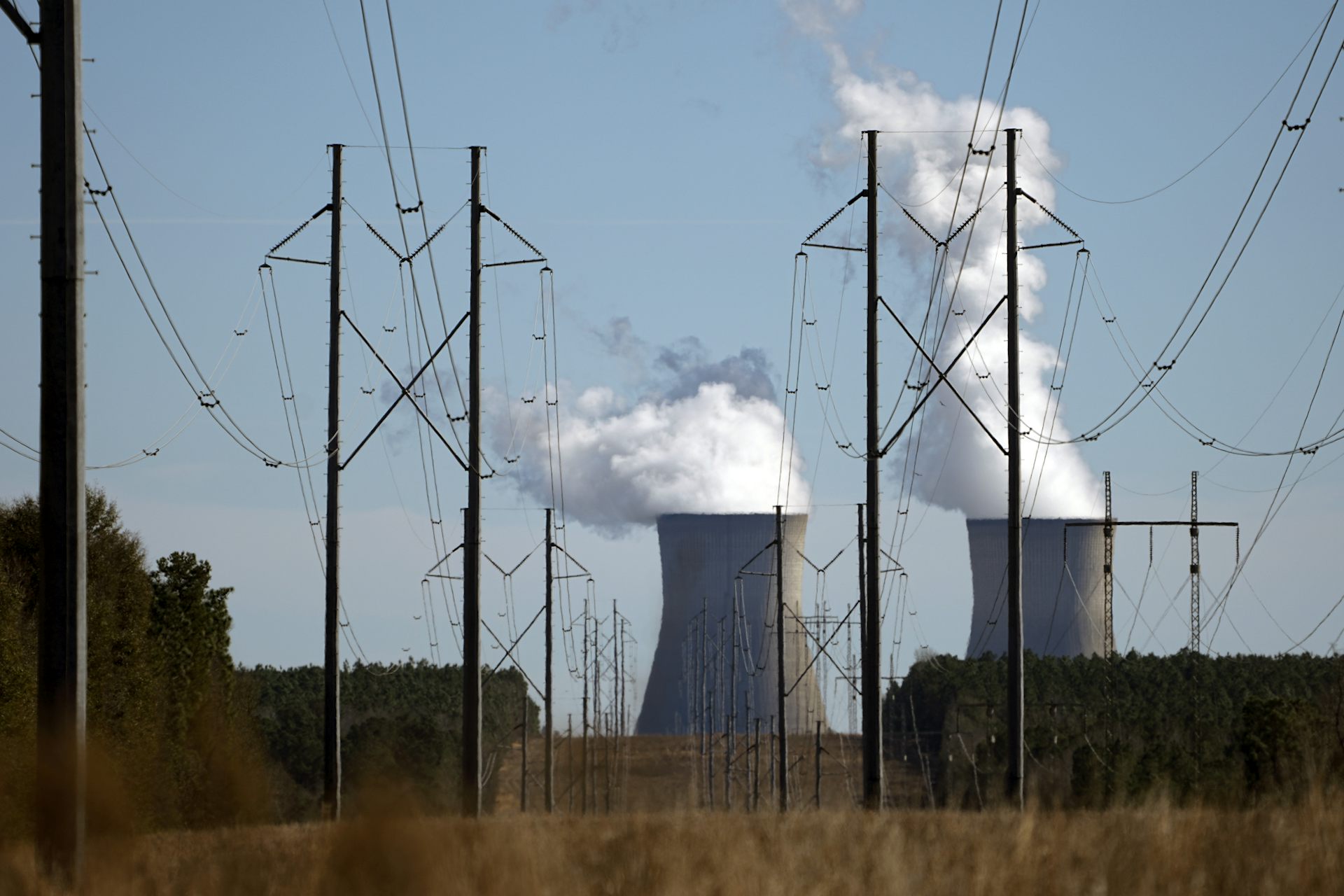 Thick columns of vapour pour from the openings of two nuclear power plant cooling towers, which are seen behind power lines