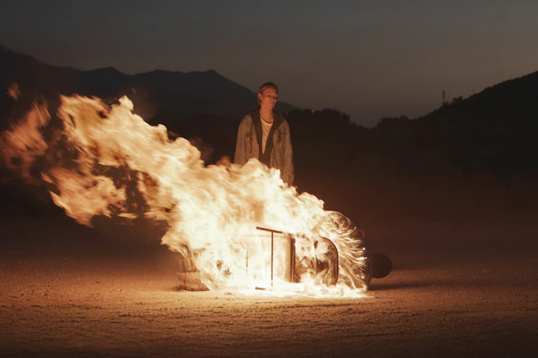 Film still: someone stands behind a burning fire.