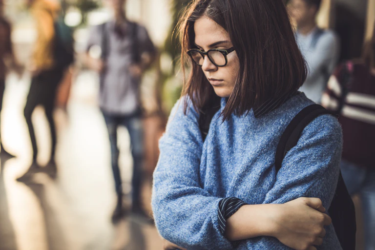 A high school girl looking sad, with other students in the background.