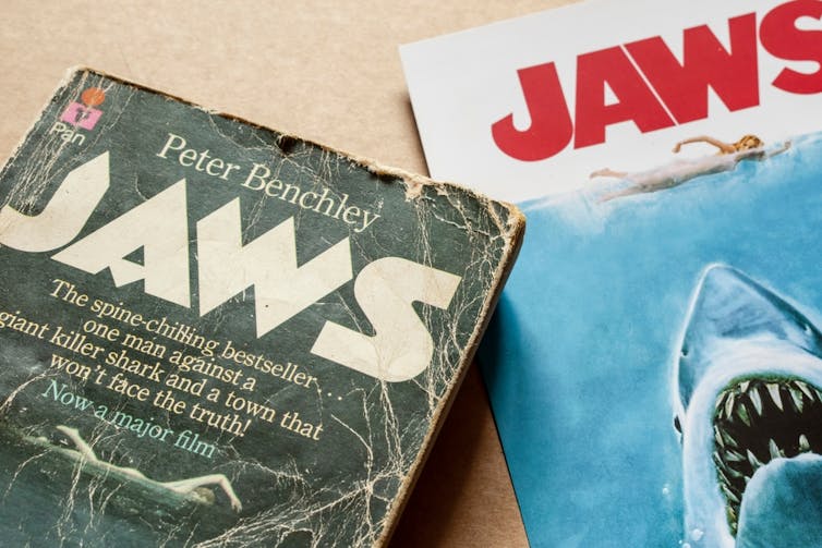 Photo of a dog-eared paperback copy of Jaws book next to a poster of the movie.