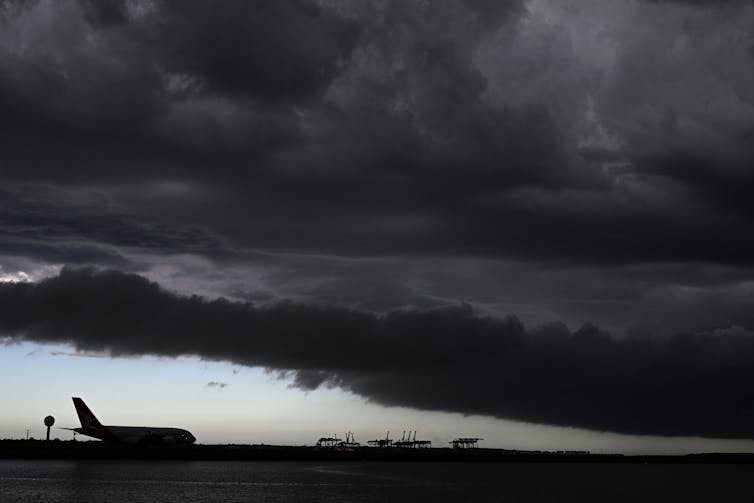 A plane taxis down the runway as dark storm clouds pass over Botany Bay in Sydney, Tuesday, February 13, 2024