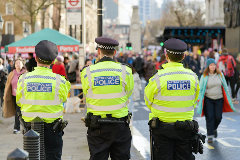 View from behind of three met police officers in high-vis jackets, looking at a busy public street
