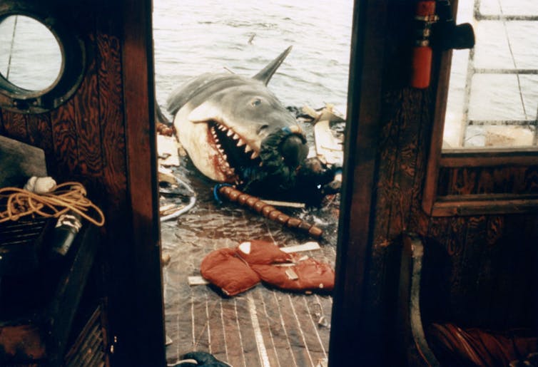 A fake shark emerging and attacking an actor on the deck of a fishing boat.